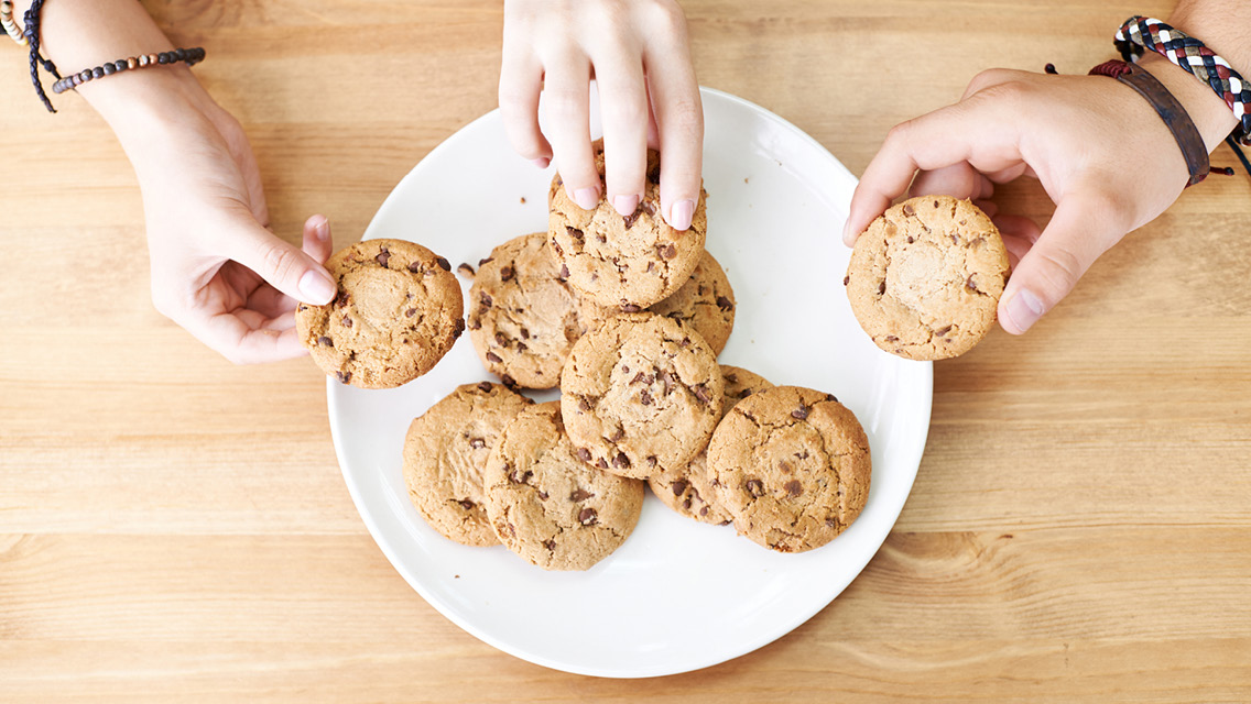 hands take chocolate chip cookies from a plate