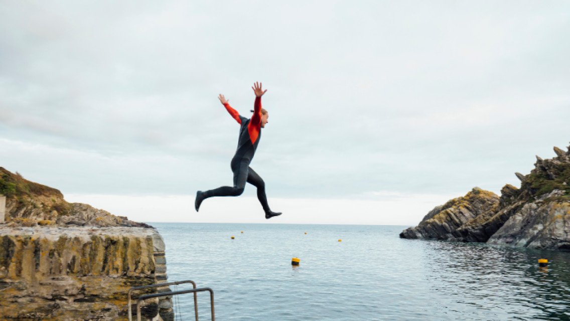 a man leaps from a cliff into water