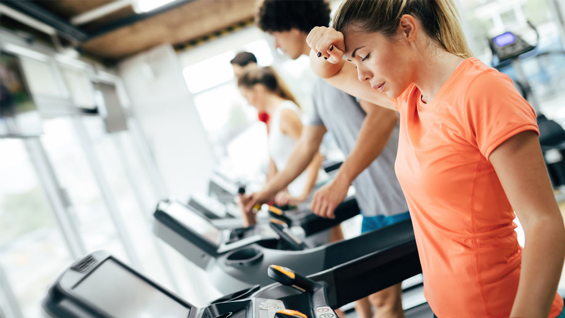 a woman wipes sweat from her brow while on a treadmill