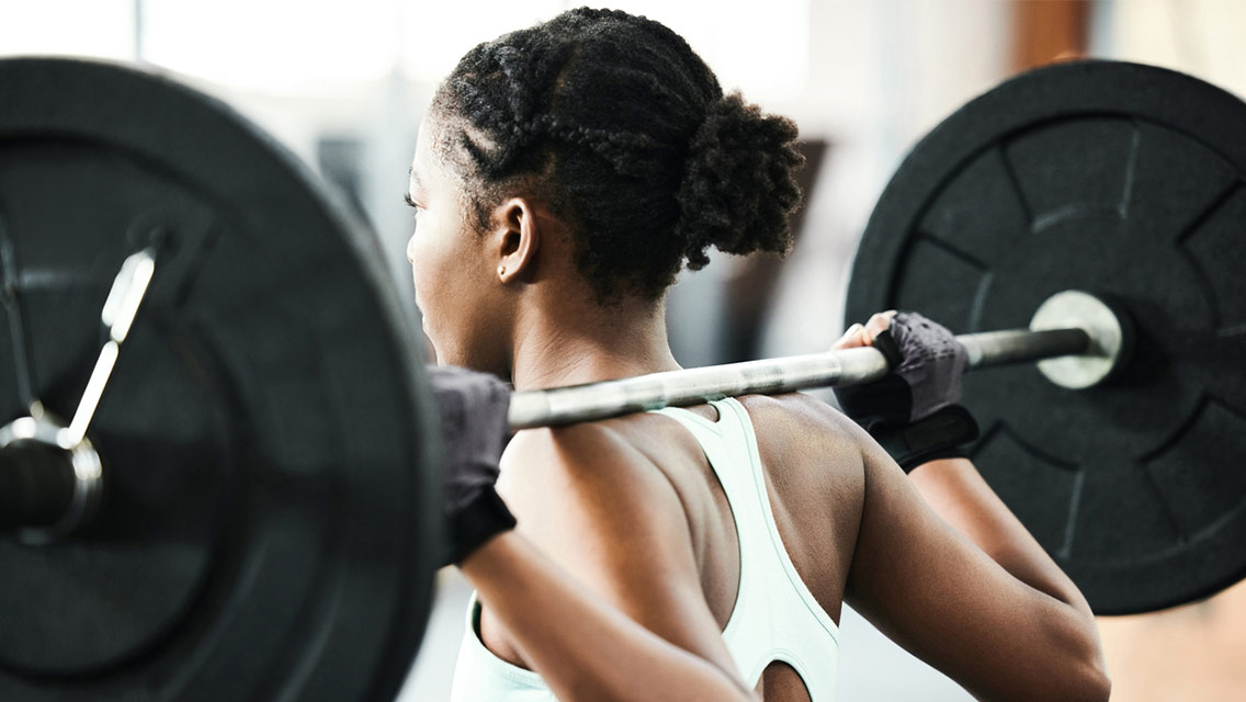a woman holds a barbell on her shoulders