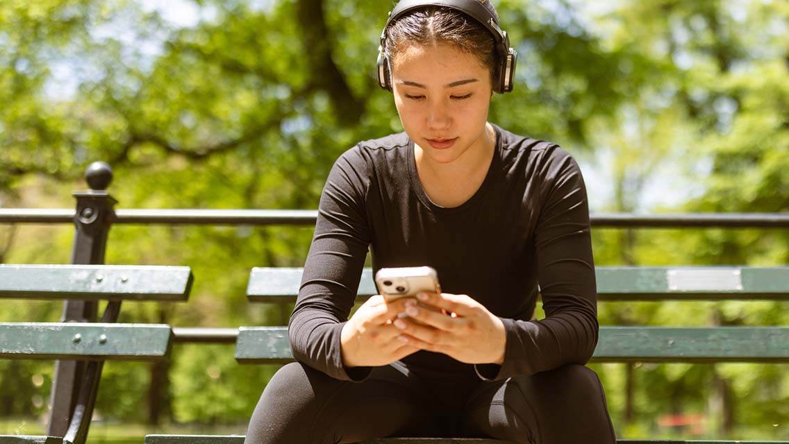 a woman sits on a park bench looking at her phone vs. working out.