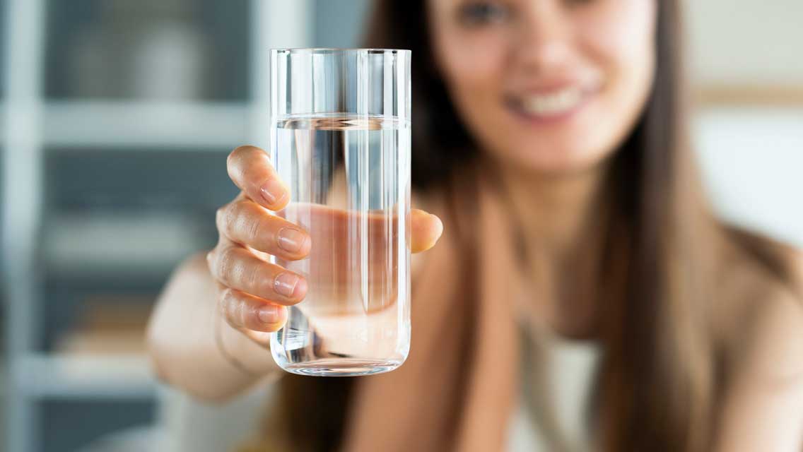 a woman holds out a glass of water