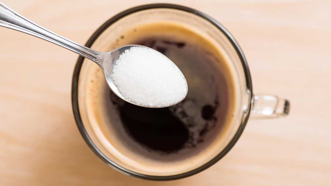 a spoon of sugar hovers over a cup of coffee