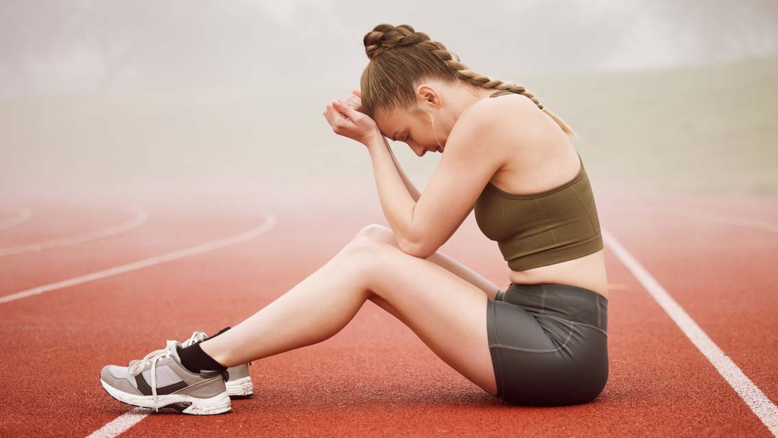 a woman athlete sits on a track with her head in her hands.