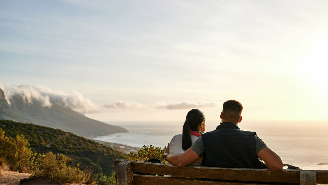 a couple sits on a park bench overlooking the ocean