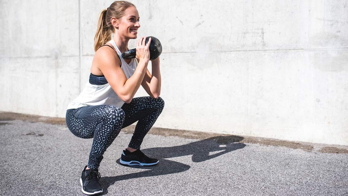 a woman performs a goblet squat with a kettlebell