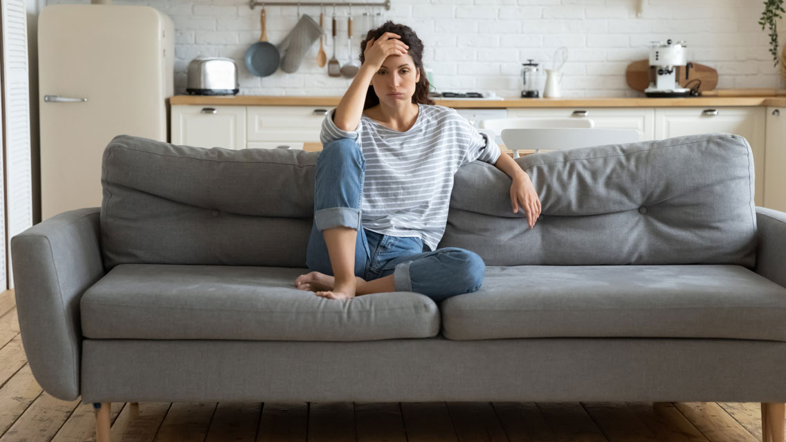 a woman sits on her couch in a posture of frustration