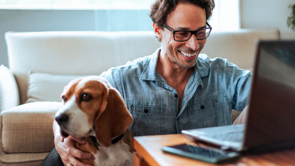 a man sits on her living room floor with his dog while working