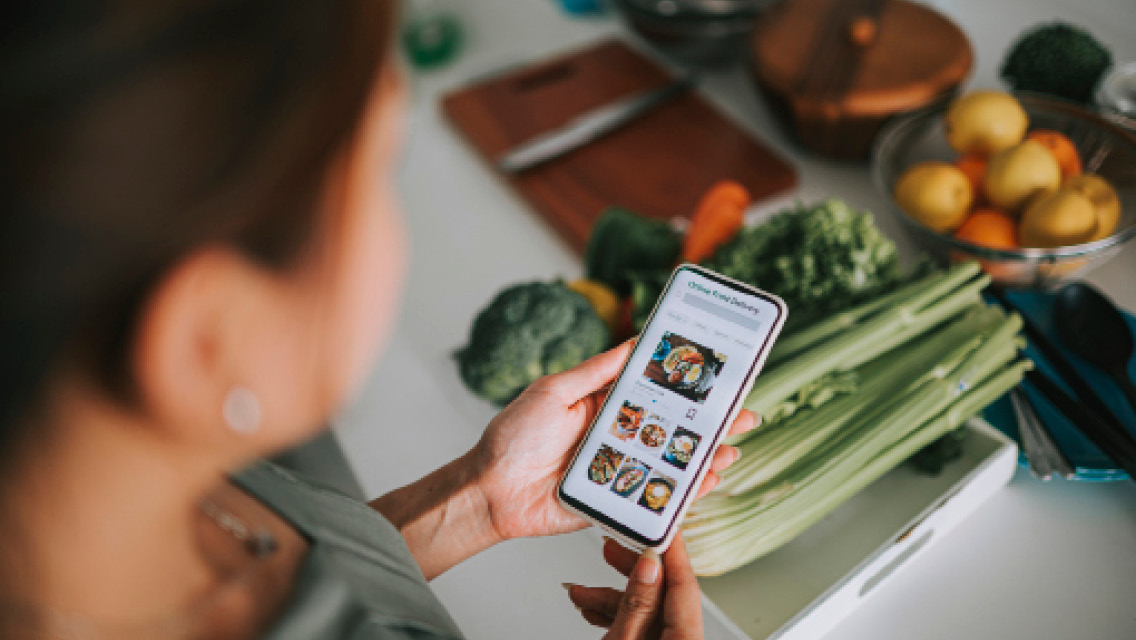 a woman looks at her phone with healthy food in the background