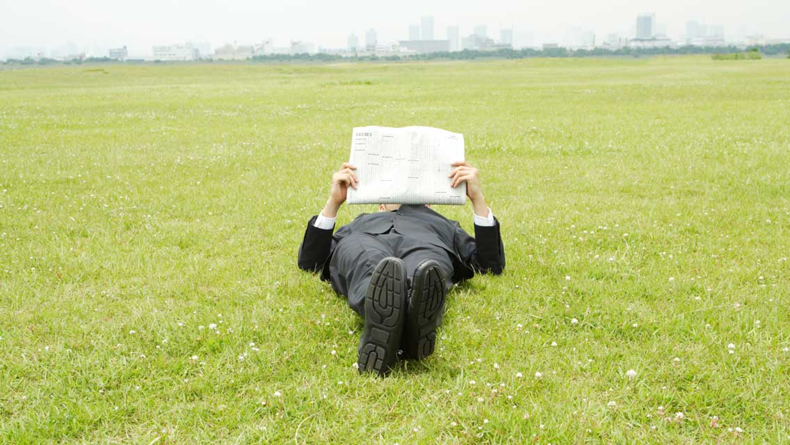 person reading newspaper lying in grass