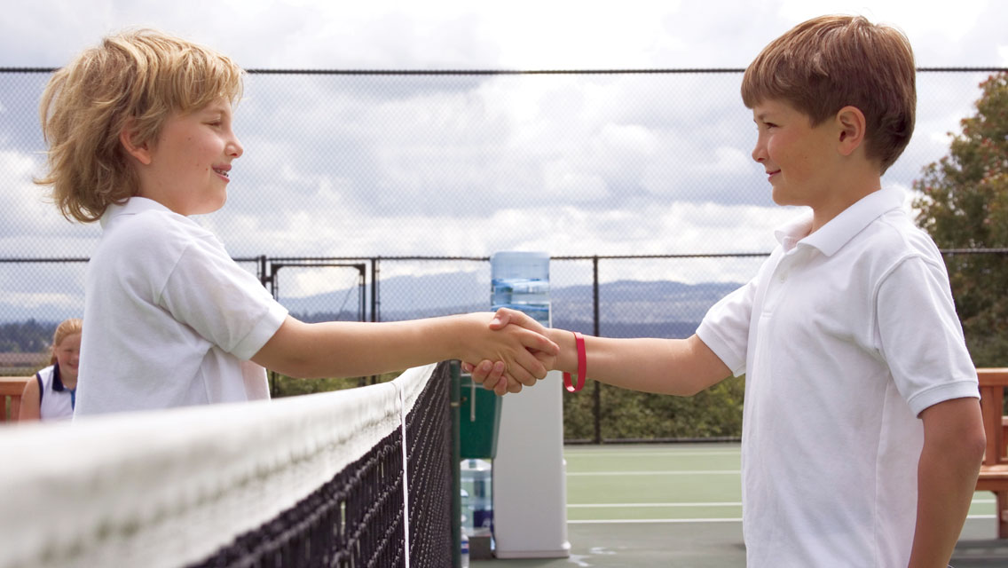 young boys shake hands at a tennis net