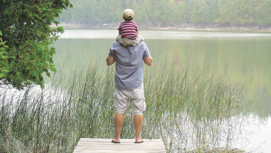 a man stands on a dock with his child on his shoulders