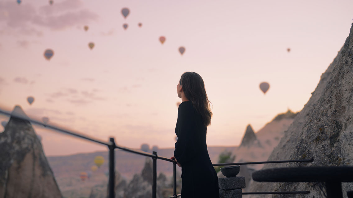 a woman watches hot air balloons rise