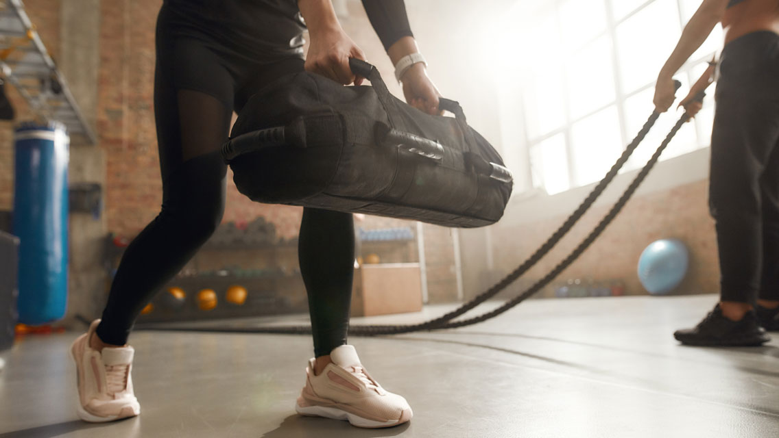 a woman lifts a sandbag in a gym setting