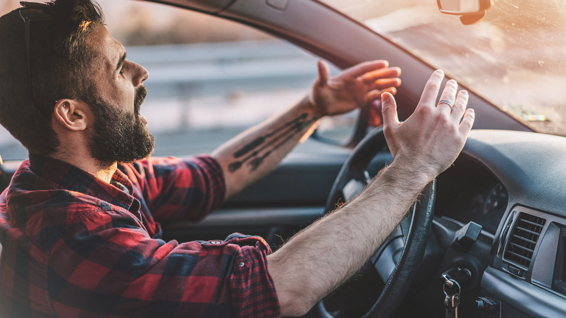 a man yells and raises his arm while driving