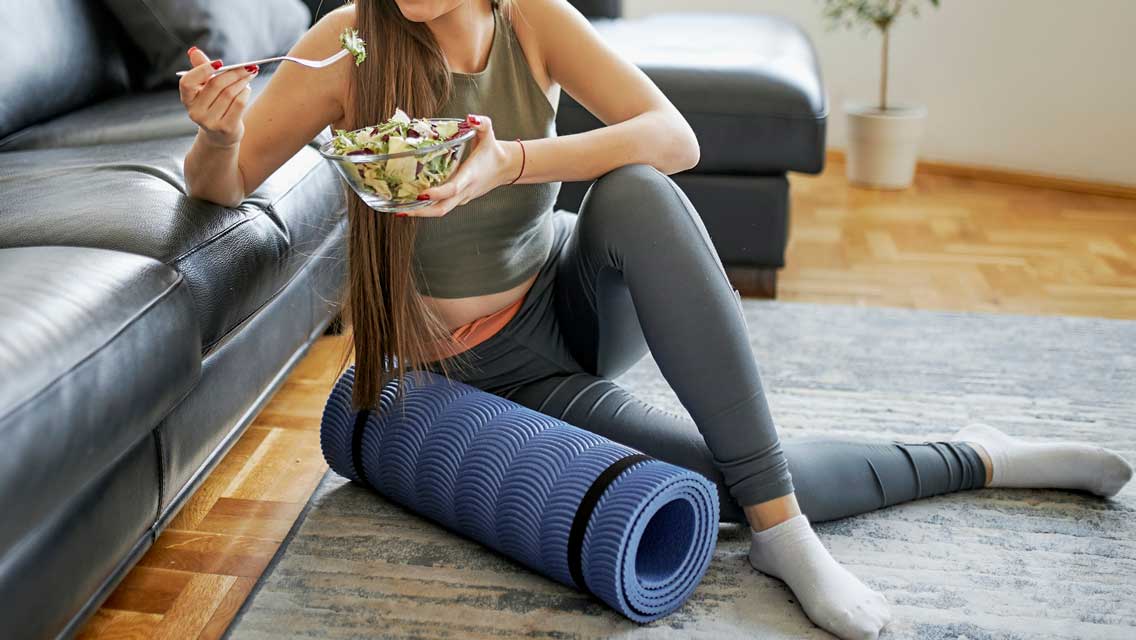 a woman eats a salad with her yoga mat next to her