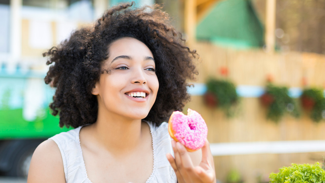 Smiling person eating a donut with pink frosting