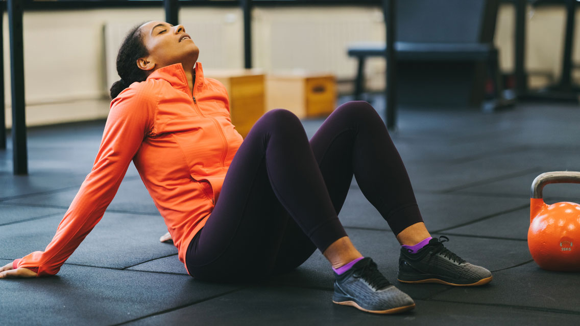 a woman sits on a gm floor, exhausted