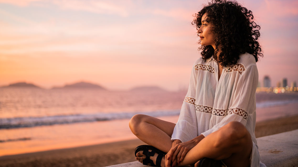 a woman sits alone watching the sunset