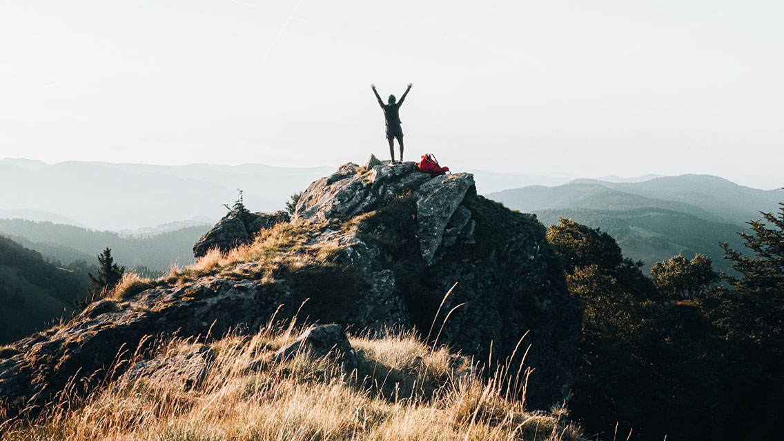 a person stands with their arms up at the top of a mountain