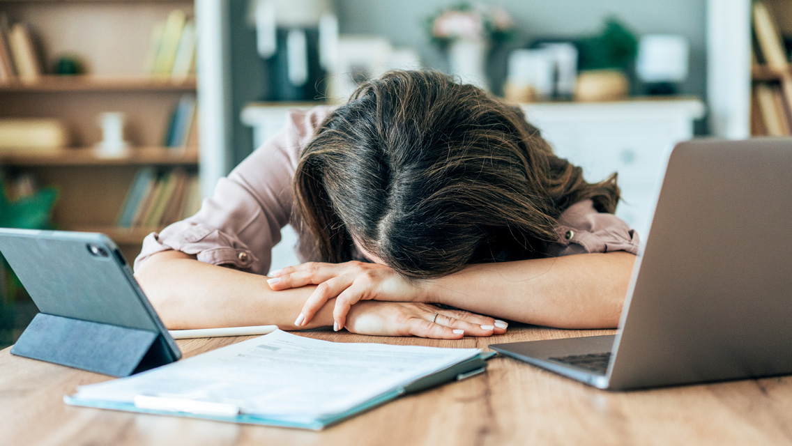 a woman sits at her desk with head in her arms, napping