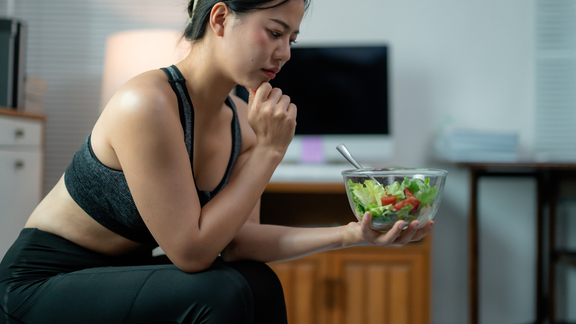 a woman looks apprehensively at a bland salad