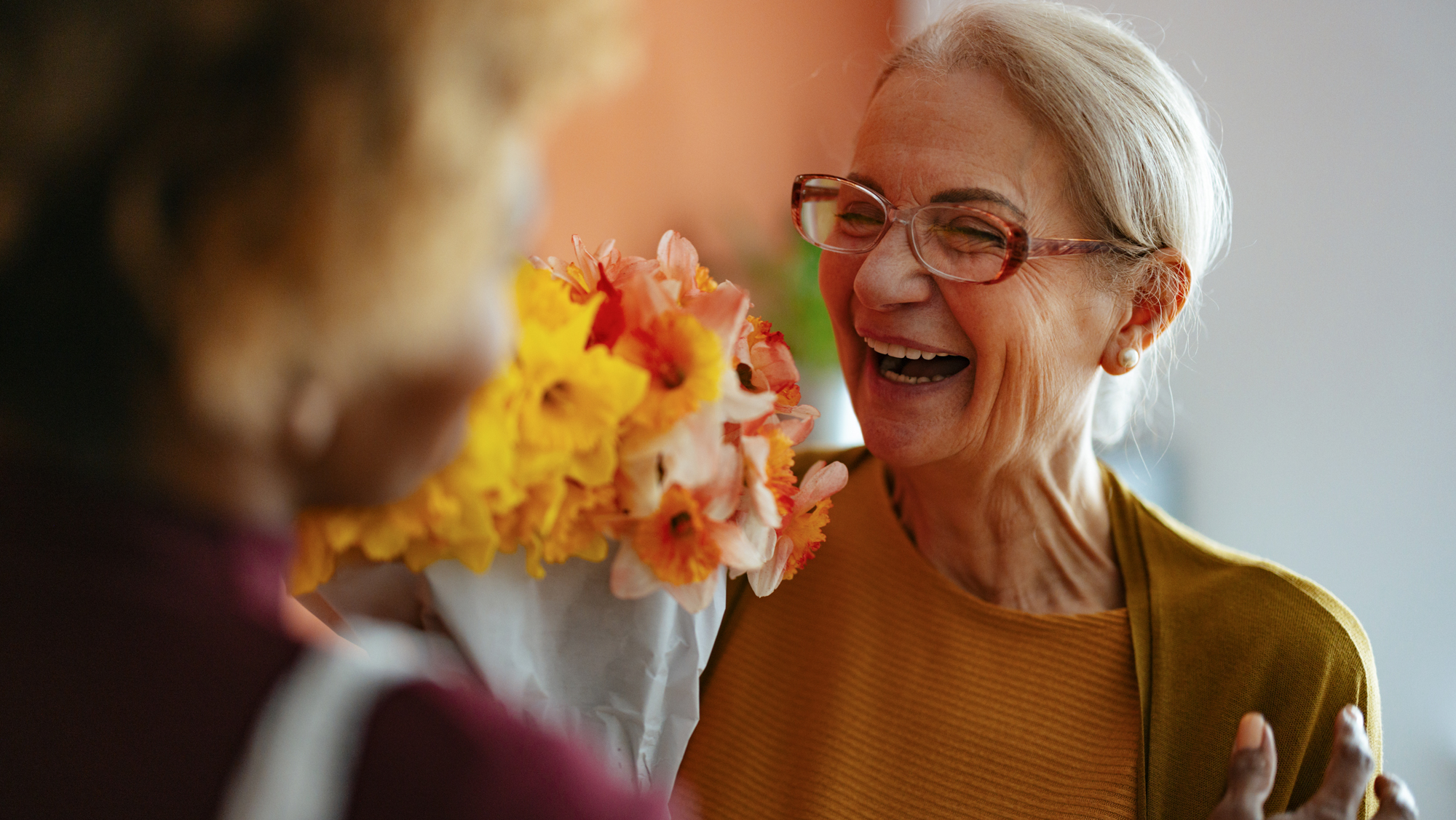 Joyful Senior Woman Receiving Flowers From Caregiver at Home