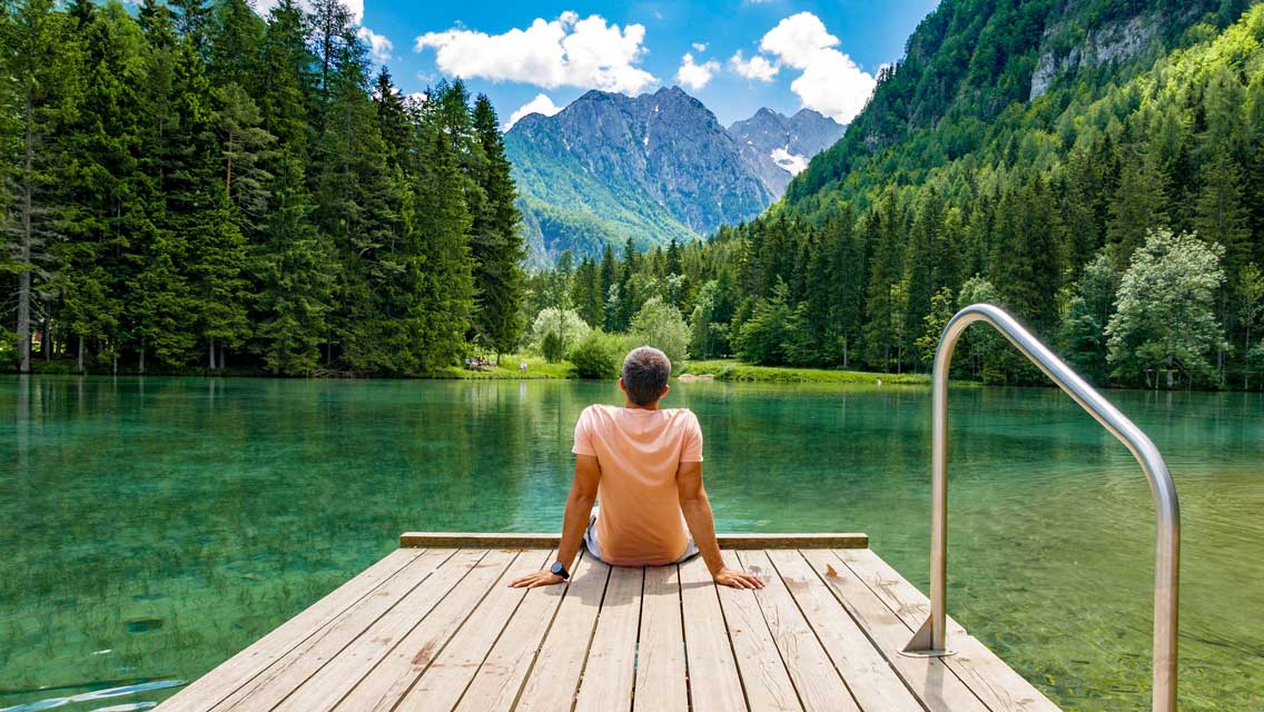 a man sits at the end of dock overlooking a beautiful mountain lake
