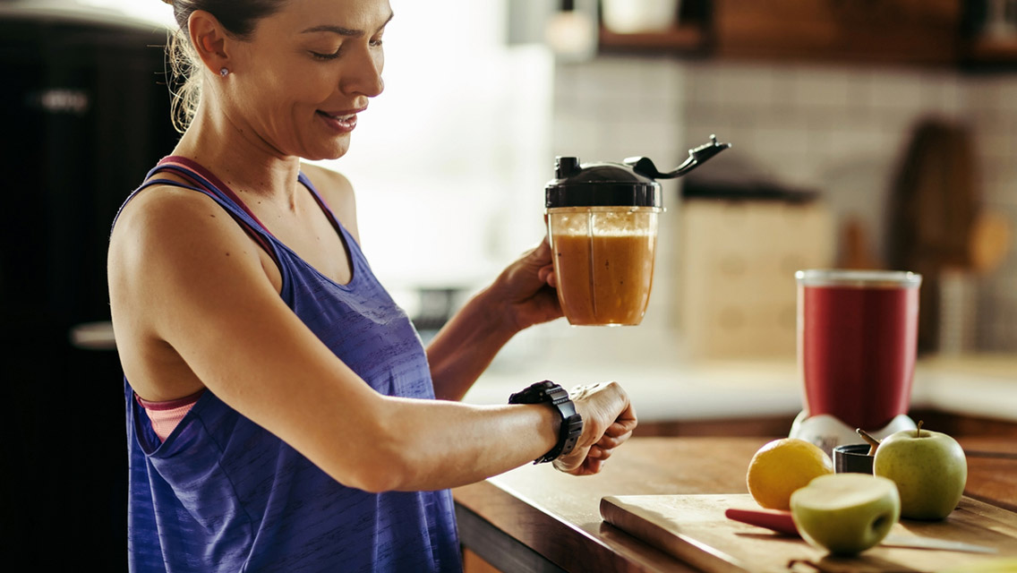 a woman looks at her smart watch while drinking a smoothie