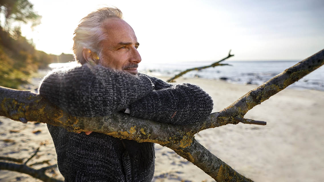 a man rests his arms over a tree branch and looks into the ocean