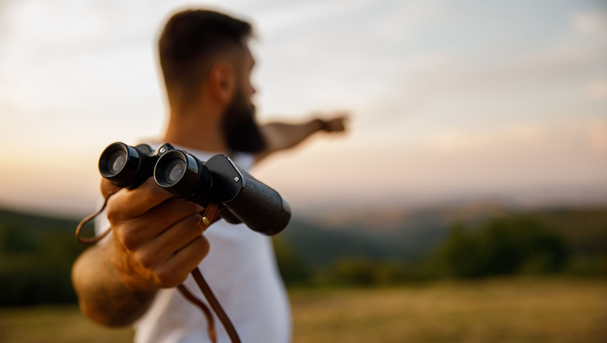 Man giving you binoculars and pointing in the distance