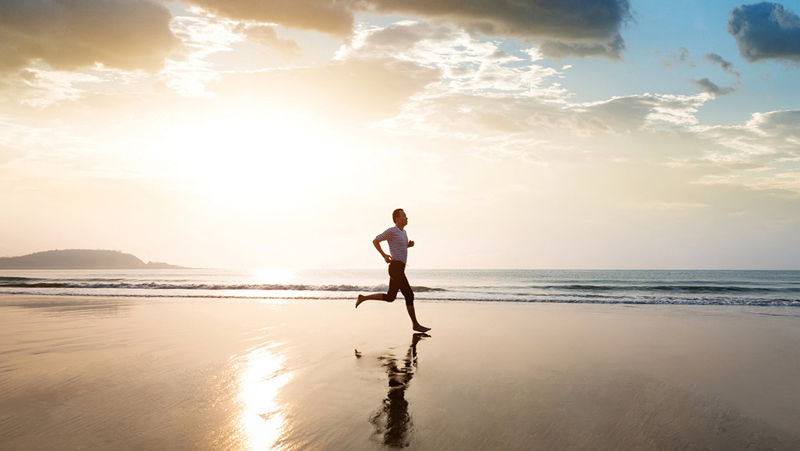 Man jogging on the beach barefoot at sunrise