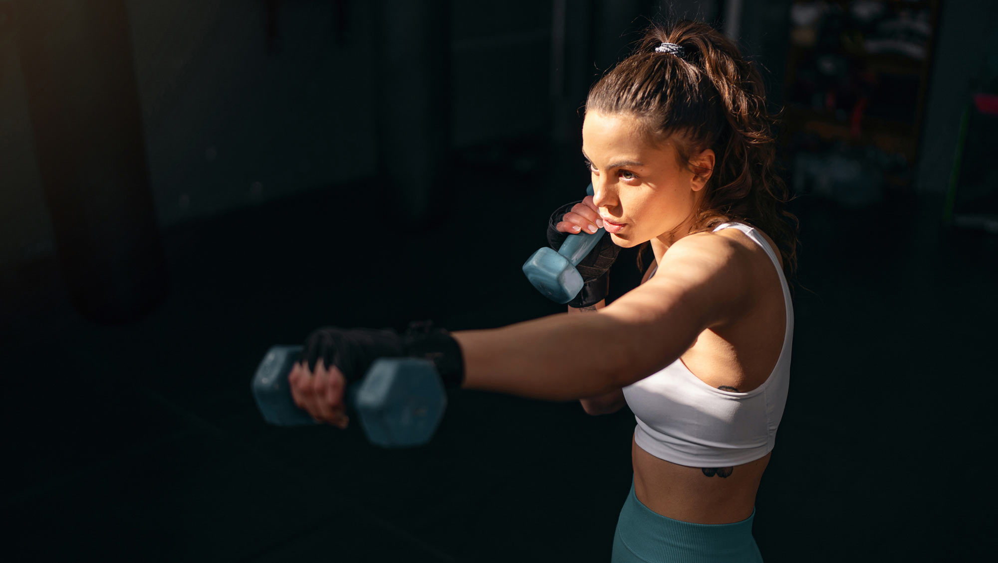 Female kickboxer shadowboxing with dumbbells