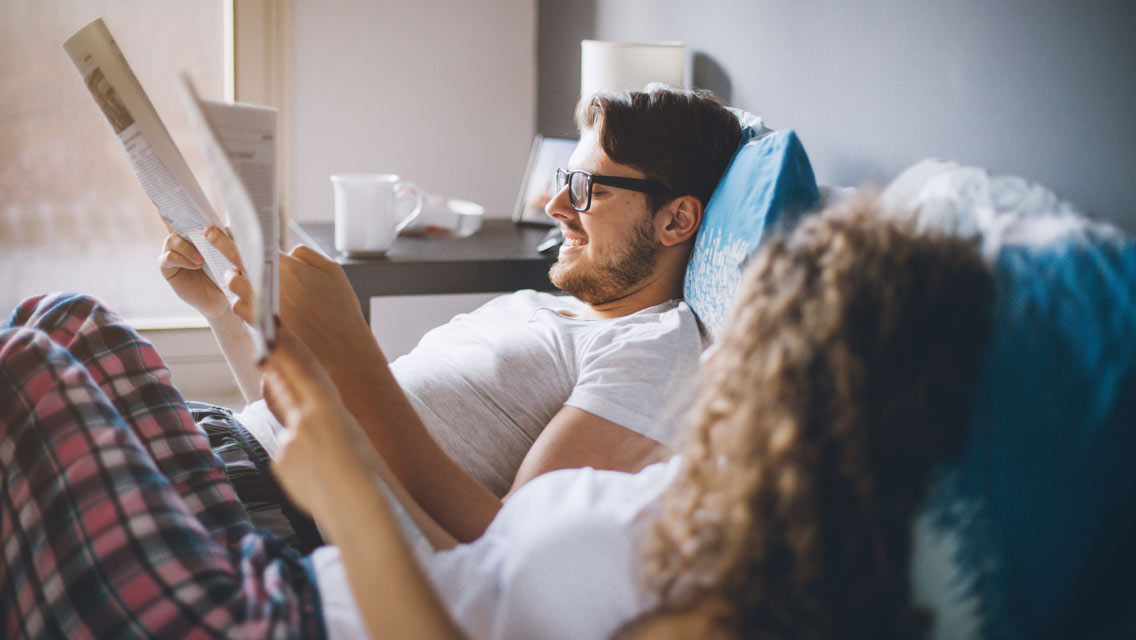 a man reads in bed next to his wife
