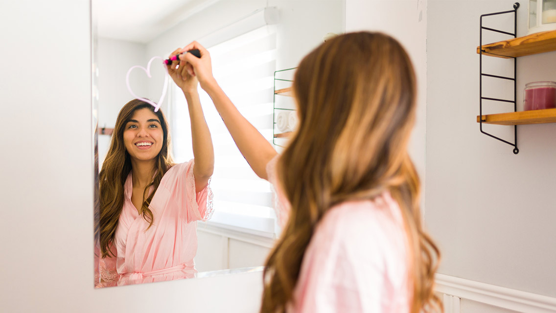 Woman drawing heart on bathroom mirror.