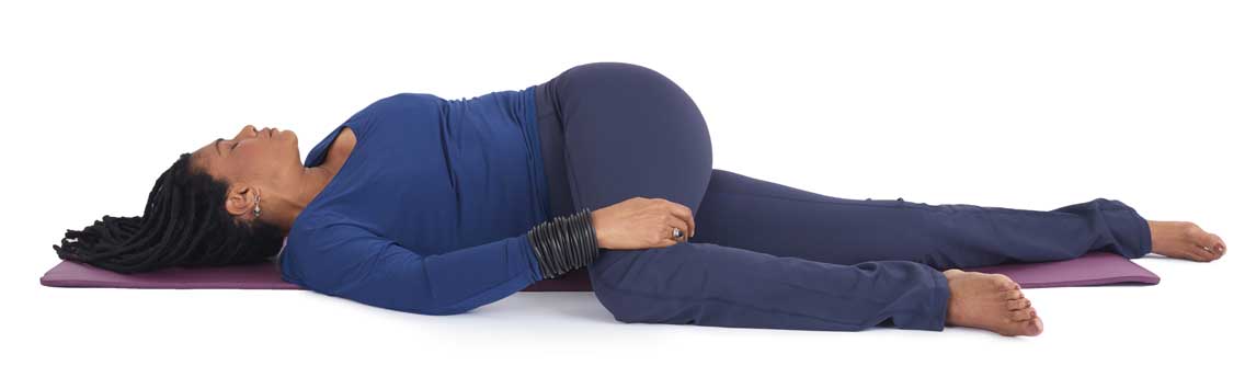 a woman lies on her back in a gentle yoga twist