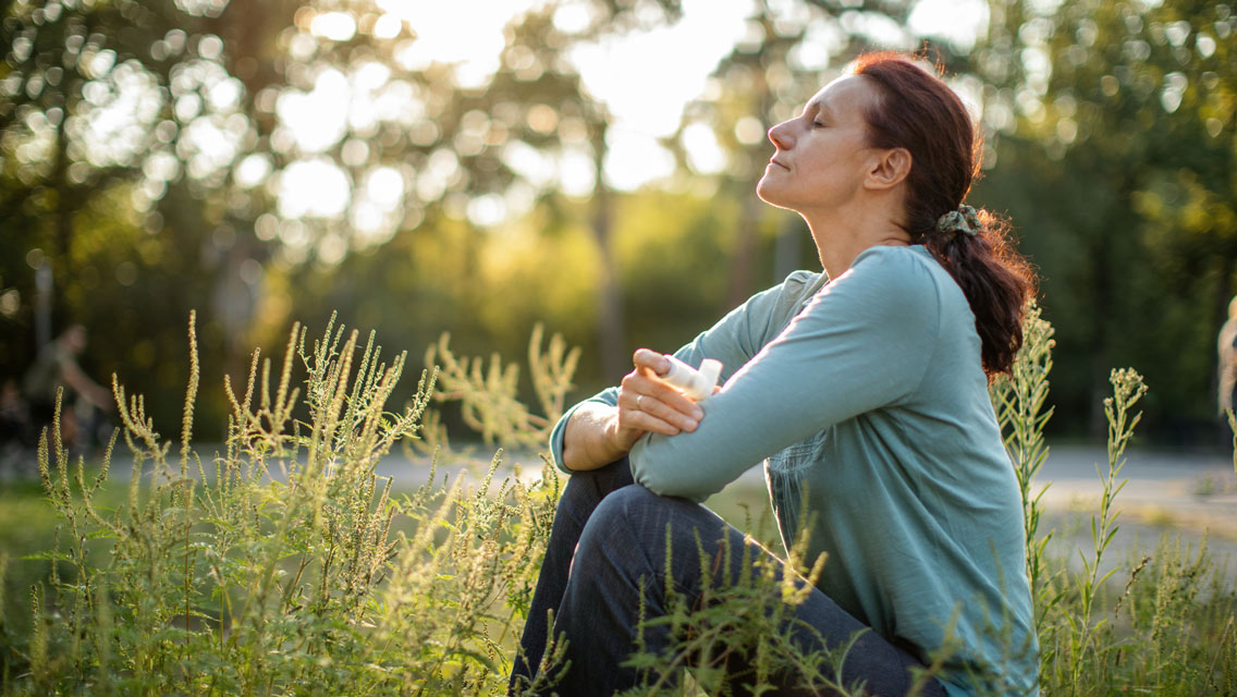 a woman sits in a park with an inhaler