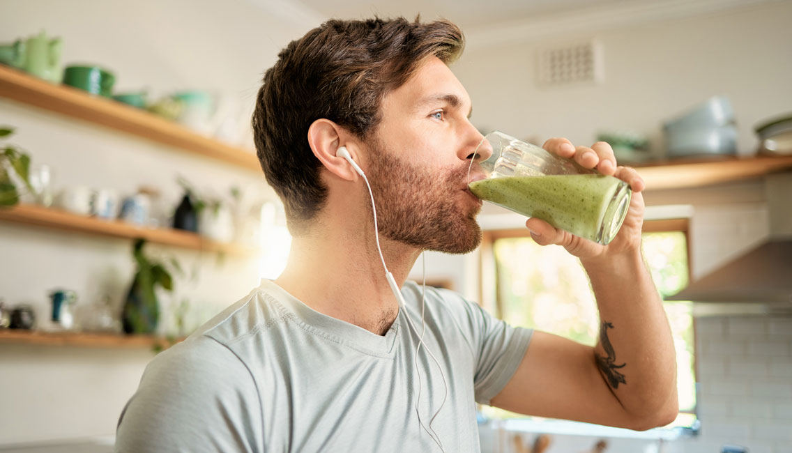 man drinking a glass of healthy green protein smoothie