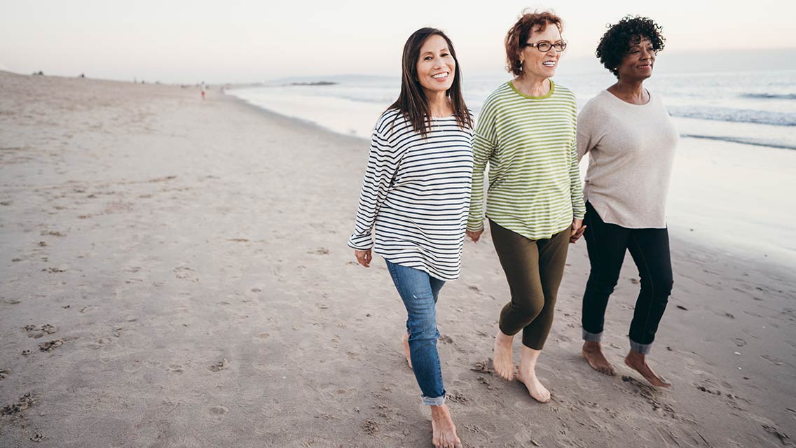 Three women are walking on the beach.
