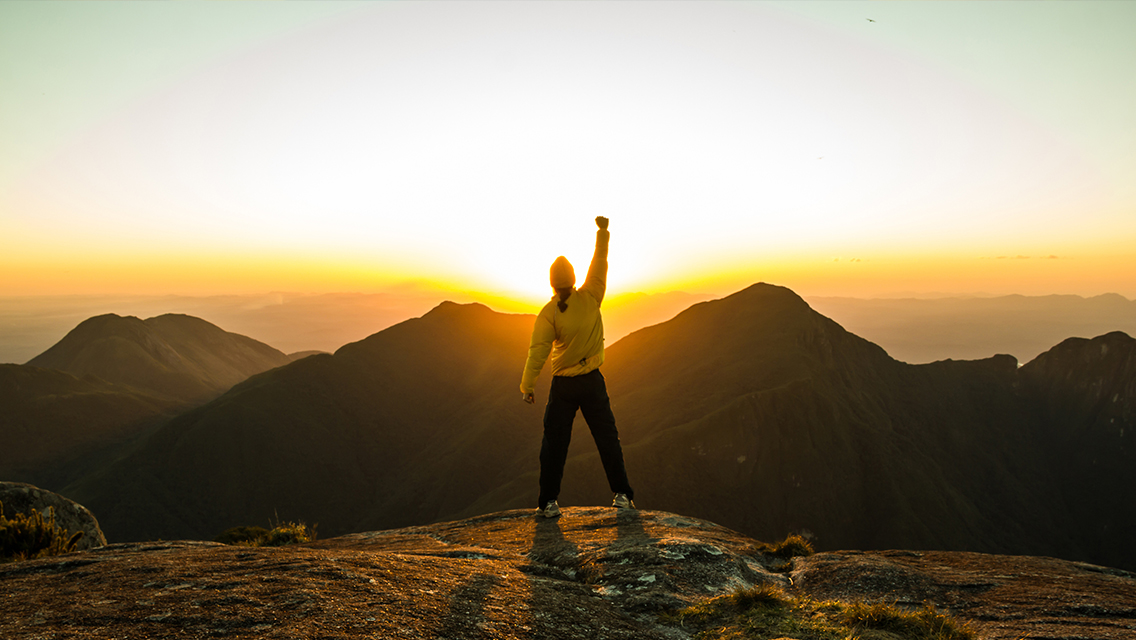 a man stands in the mountains at sunset with his arm raised to the sky