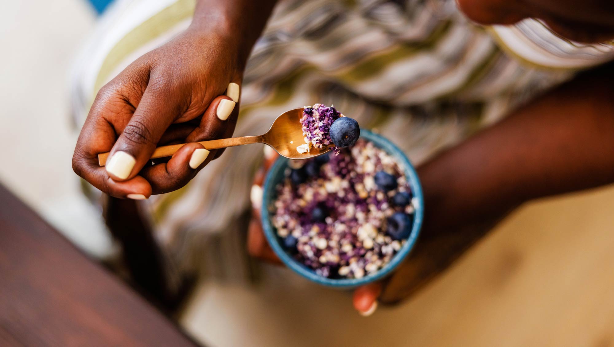 a woman eats a small bowl of oatmeal with blueberries