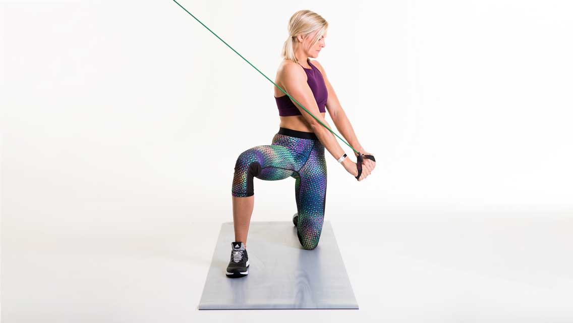 a woman pulls a band down and across her body while in a lunge position