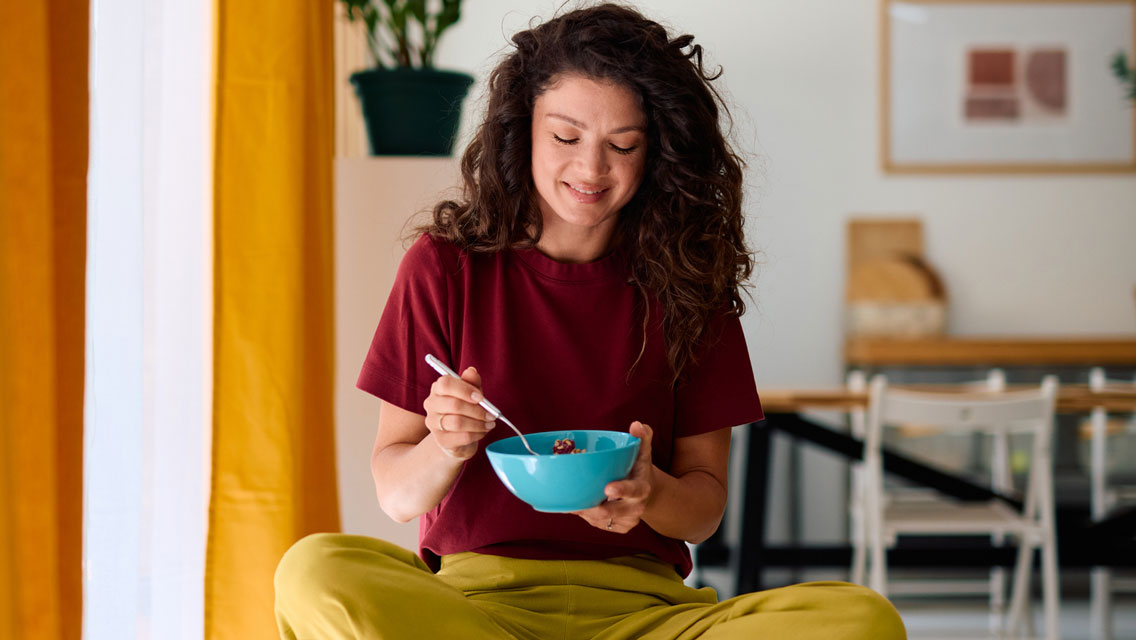 a woman sits crosslegged enjoying breakfast in the morning light
