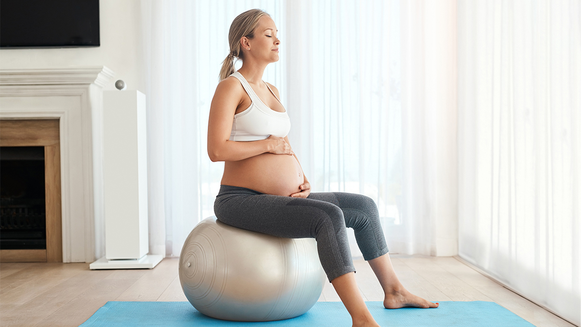 a pregnant woman sits on a swiss ball