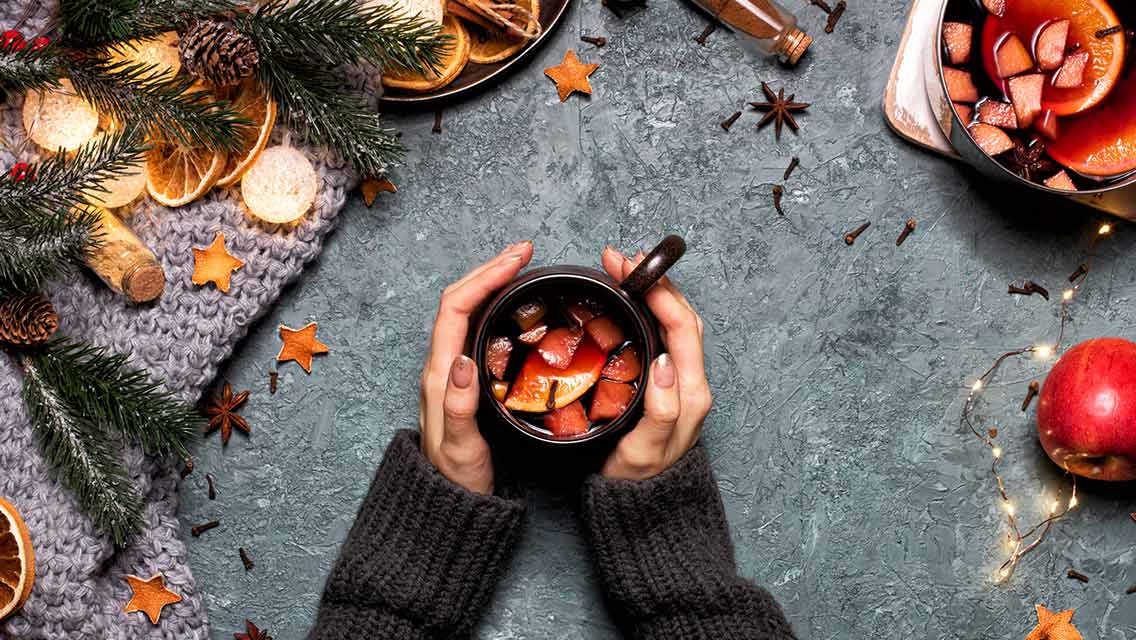 hands hold a mug filled with a winter sangria surrounded by seasonal items