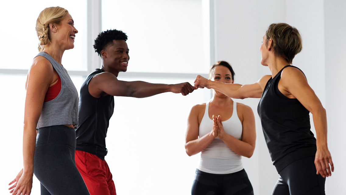 A group of four people in a fitness facility with two of them fist bumping.