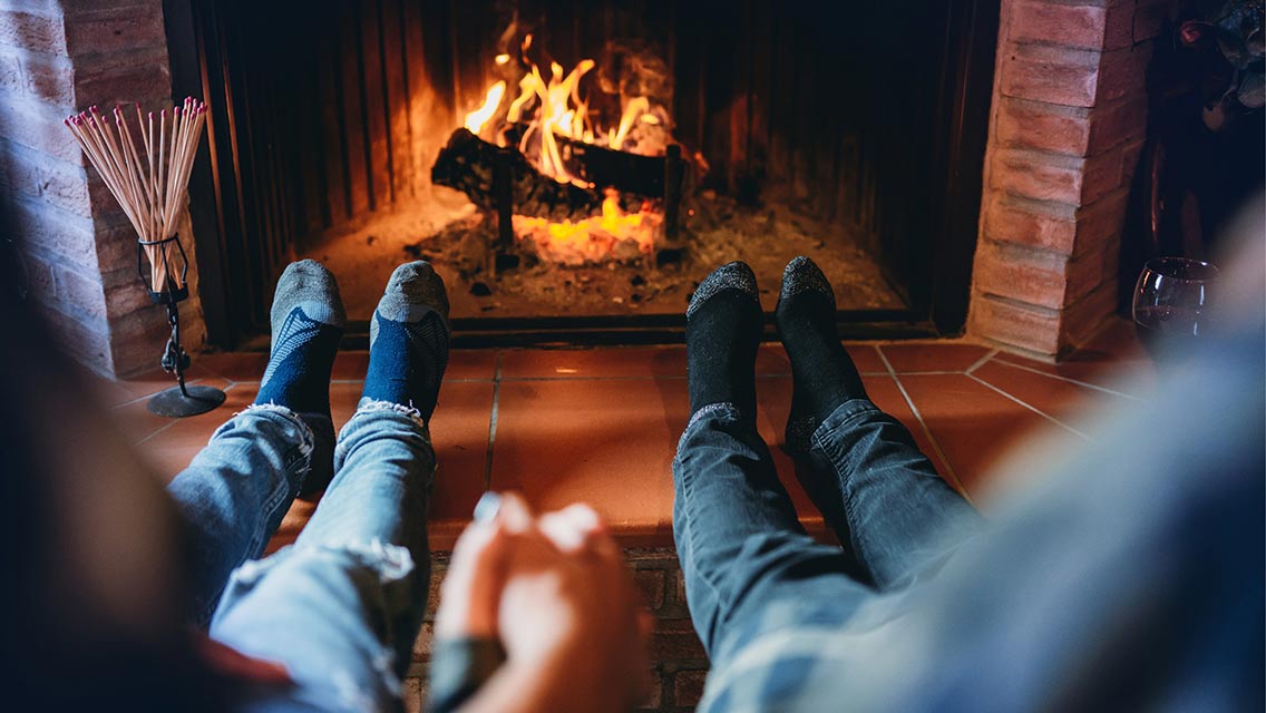 a couple sits holding hands with their feet at a fireplace