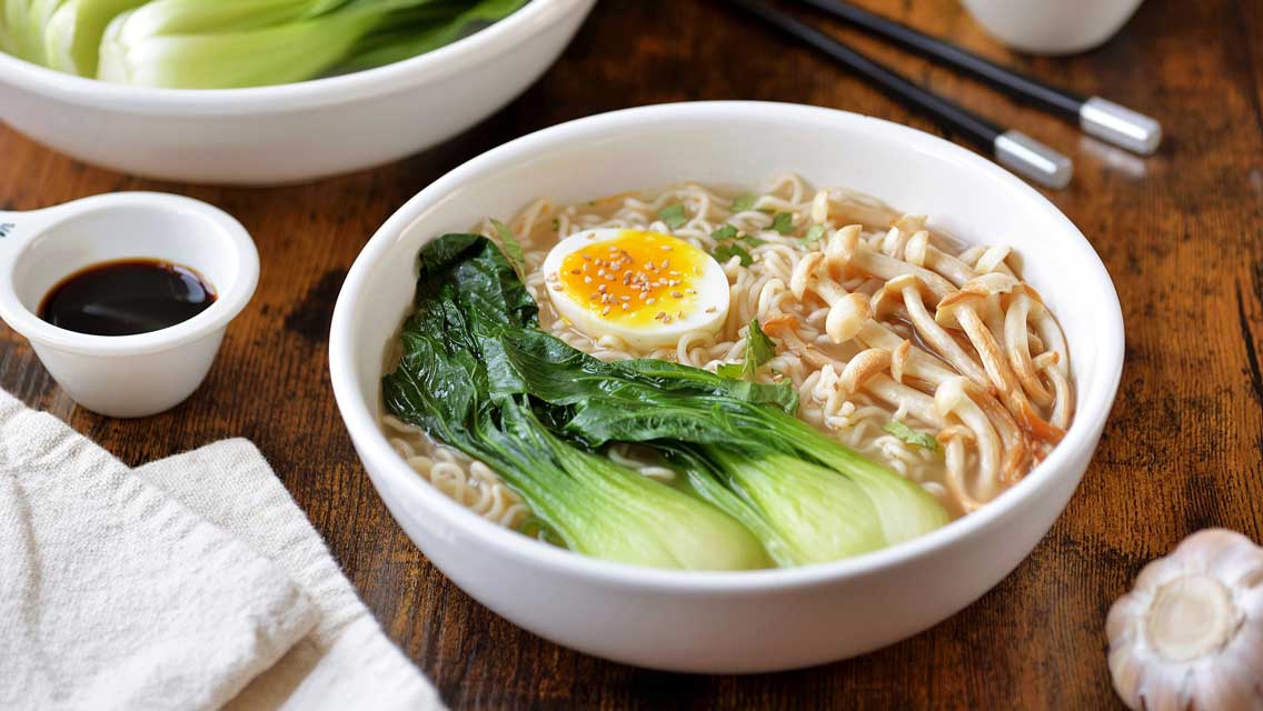 a bowl of ramen with bok choy, mushrooms, and a hard boiled egg