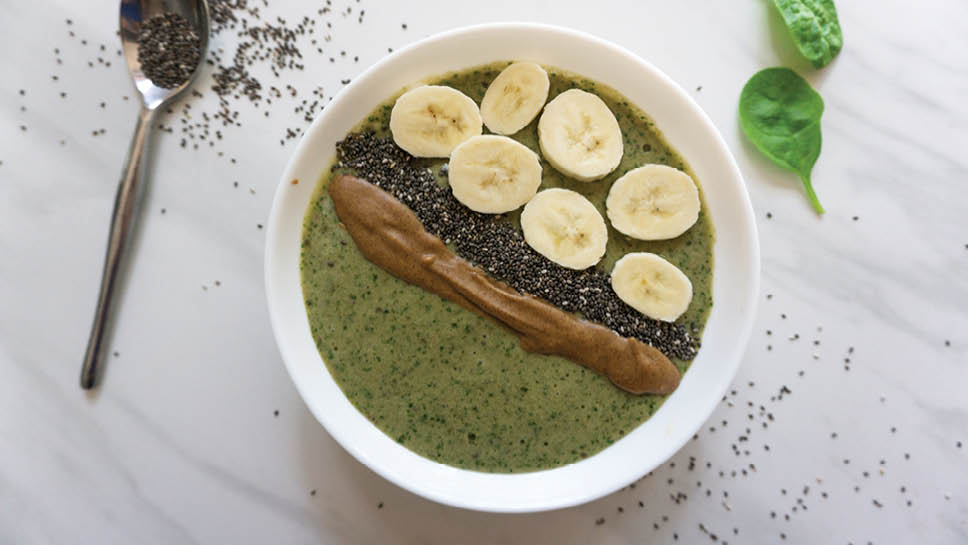 A green smoothie bowl topped with peanut butter, chia seeds, and banana slices is pictured.