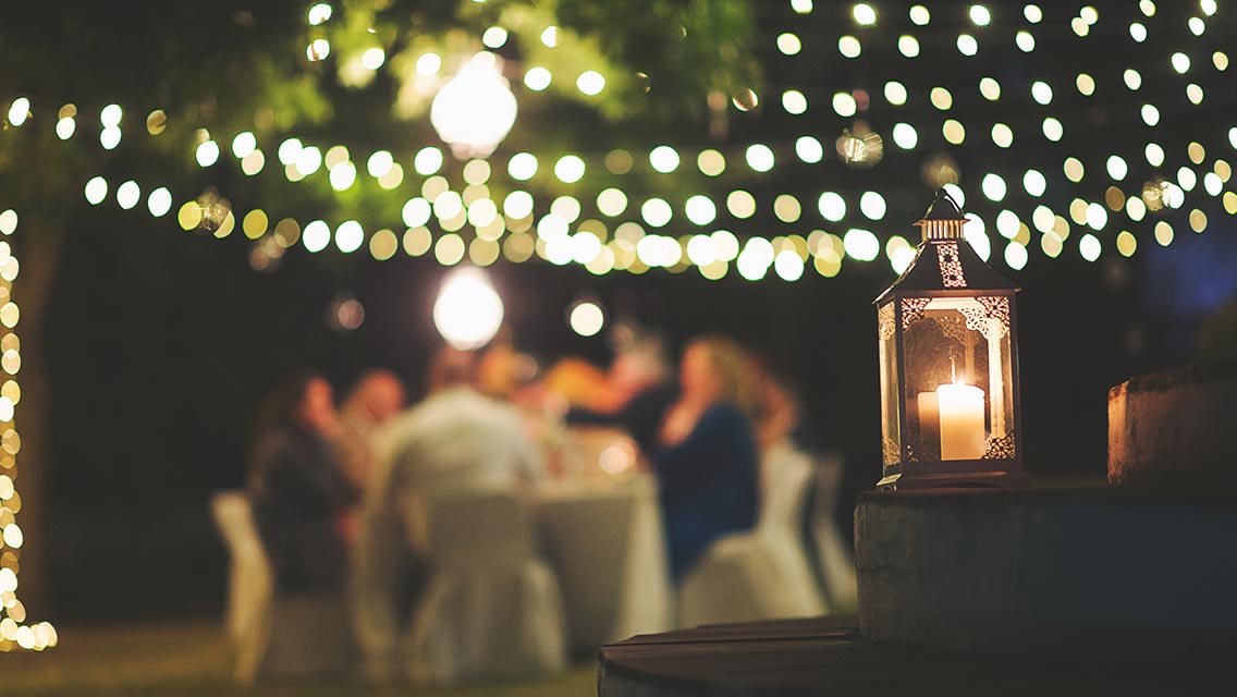 Candle and string lights in front of outdoor dinner party